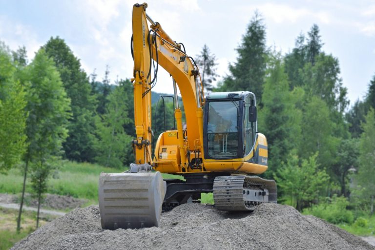 A yellow excavator on a pile of gravel in a lush, green forest setting in Poland.